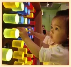 Toddler playing with a light-up tube wall at a children's museum