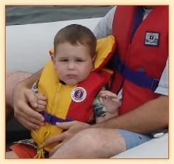 Toddler wearing a yellow life jacket on a boat with a parent