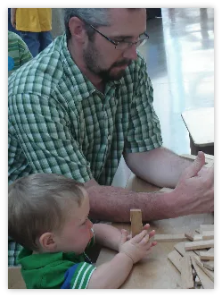 Dad helping a toddler build with wooden blocks