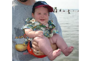 Smiling baby in a Hawaiian shirt held up at the lake