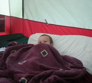 Child tucked into a sleeping bag inside a tent