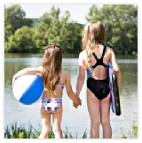 Two girls in swimsuits holding hands by a lake with a beach ball