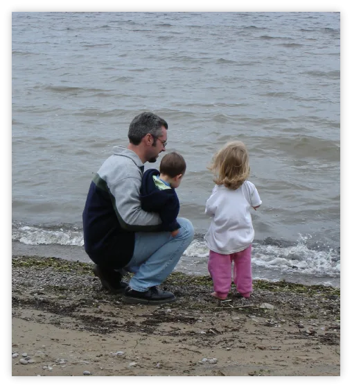 Dad crouching with two young children at the water's edge